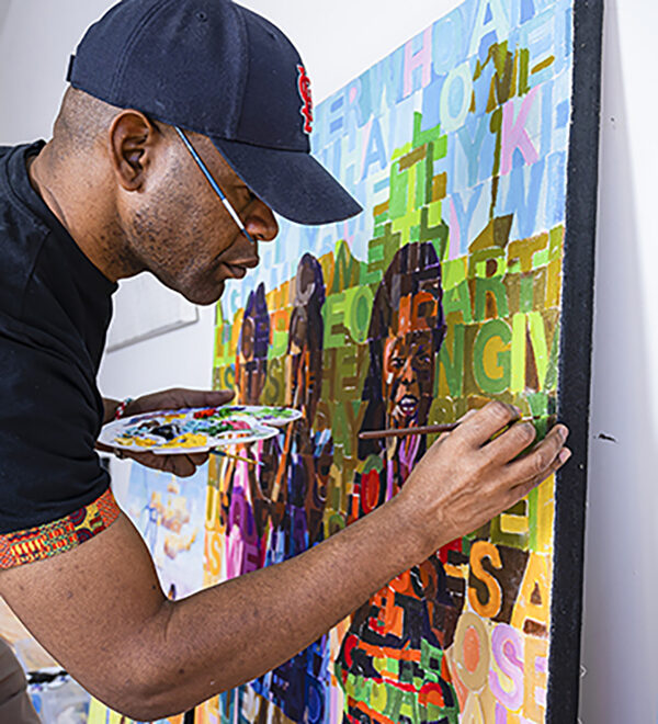 WashU alumnus, Paul Banda painting on a large colorful canvas