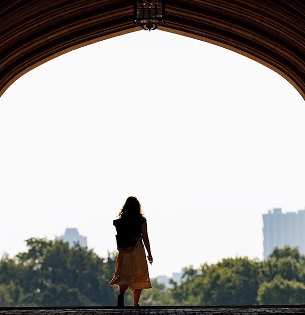 Woman walks under archway of Brookings Hall at WashU